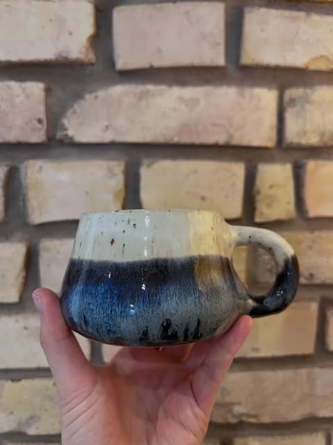 Eine Tasse mit tiefblauer und heller Glasur vor einer Backsteinwand