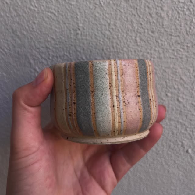 Ein Keramikbecher mit rosa, grünen und cremefarbenen Glasurstreifen